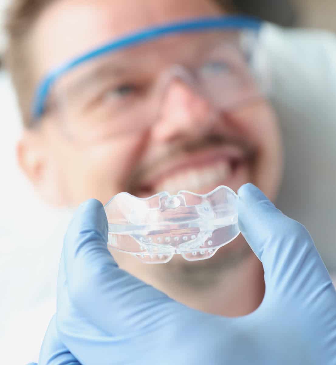 Dentist tries on silicone mouthguard to patient.