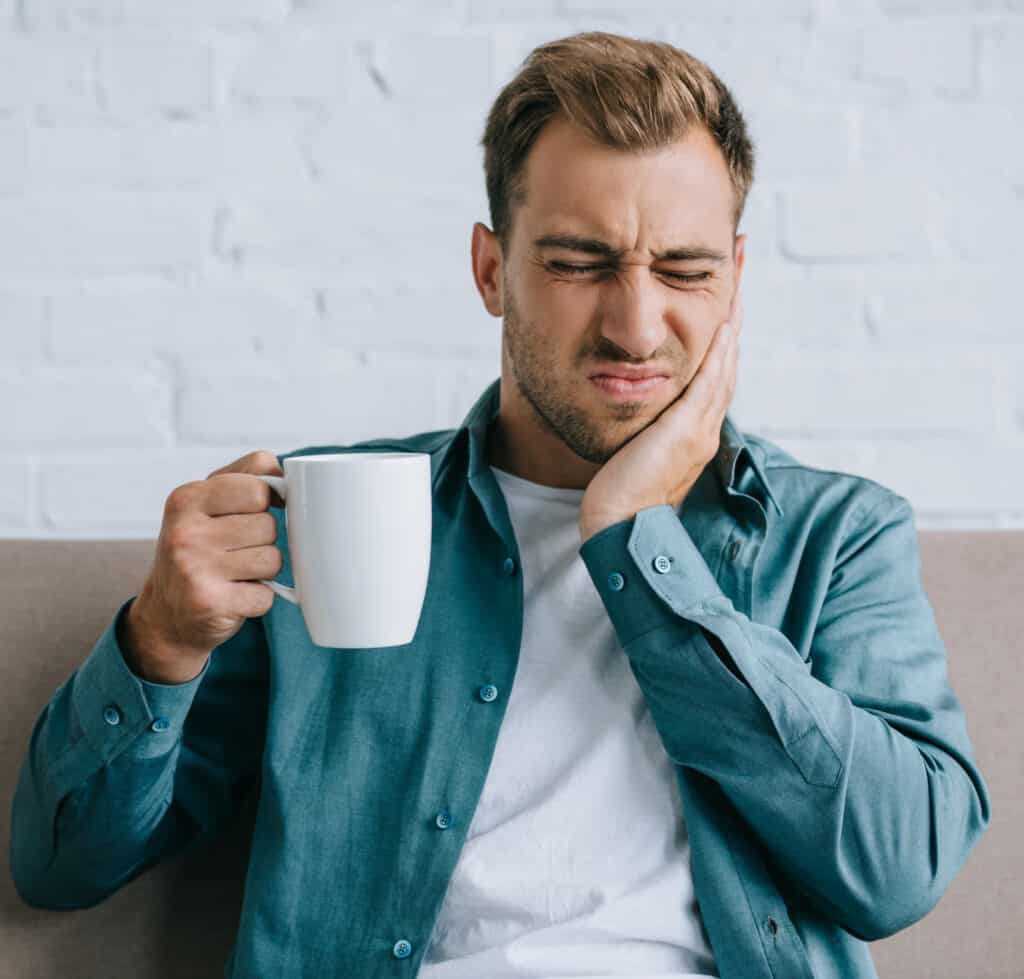 Why Are My Teeth Sensitive? Causes and How to Treat It 1 Woman holding her cheek from tooth sensitivity while drinking a cold beverage