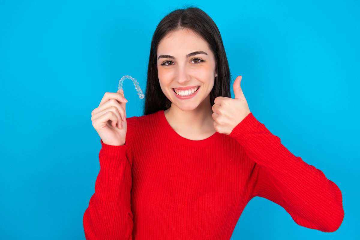 woman holding invisible braces aligner rising thumb-up recommending-this-new-treatment-dental