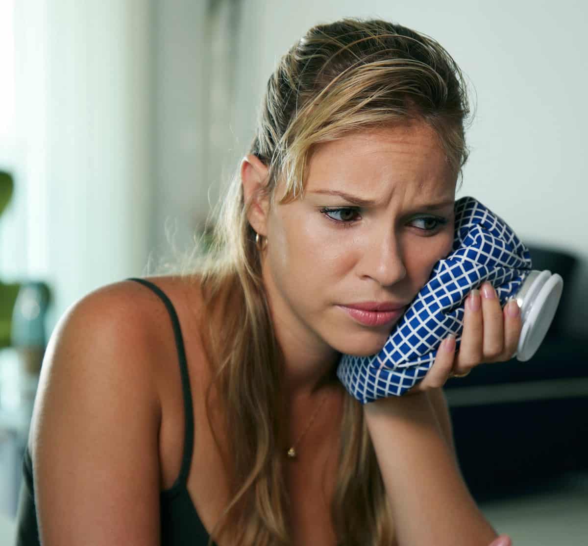 Young woman with toothache holding ice bag on cheek - emergency dentist